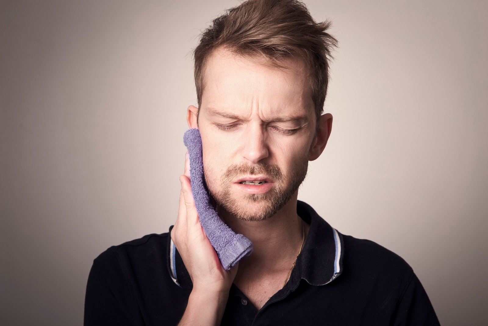 A man holding a cold pack against his jaw in discomfort